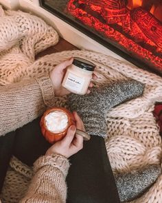 a woman is holding a jar of whipped cream while sitting in front of a fireplace