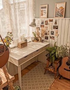 a room with a desk, guitar and plants in it