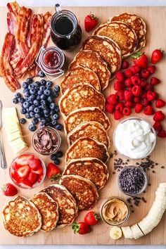 pancakes, strawberries, blueberries, and other foods are laid out on a cutting board