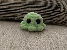 a small green stuffed animal sitting on top of a bed next to a black and white pillow