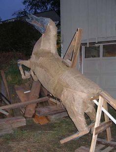 a wooden horse that is standing on some wood planks in front of a garage