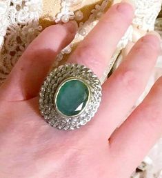 a woman's hand holding a ring with a large green stone in the middle