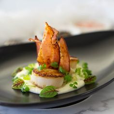 a black plate topped with scallops covered in sauce and garnished with green leaves