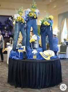 two blue jeans are standing on top of a table with flowers and hats around them