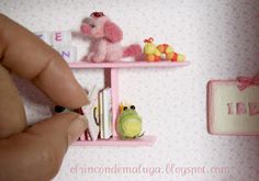 a hand is holding a tiny doll in front of a shelf with toys on it