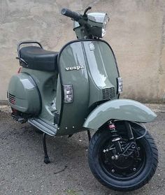 a green scooter is parked in front of a stone wall and has the word vespa written on it