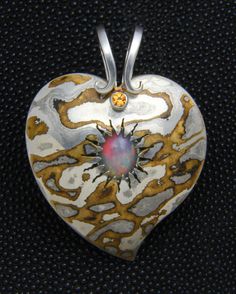 This heart pendant is made from Mokume Gane, a process of metal fabrication that dates back to the age of the Samurai. It involves fusing two or more alloys that are then carved, twisted, sanded, or otherwise manipulated to produce a pattern similar to wood grain. In this case, the metals I used were sterling silver, brass, and a Japanese alloy called Shibuichi. In the center, as though bursting from a volcano, is an African Welo Opal. The accent stone at the top, beneath the scrolls in the bail, is a faceted citrine. The pendant measures 2 inches from the tip to the top of the bail. Artisan Heart-shaped Jewelry For Anniversary, Unique Hand Forged Heart Pendant, Unique Hand Forged Heart Pendant Jewelry, Artisan Heart Pendant Jewelry, Unique Hand Forged Necklace With Heart Pendant, Unique Hand Forged Heart-shaped Jewelry, Artisan Silver Heart Jewelry, Artisan Silver Heart-shaped Jewelry, Artisan Silver Heart Pendant Jewelry