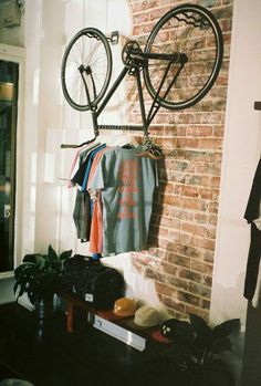 a bicycle hanging on a brick wall next to a coat rack with clothes and hats