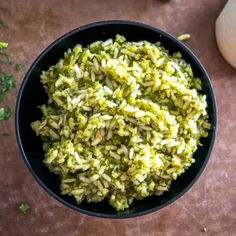 a black bowl filled with green rice next to an onion and broccoli florets