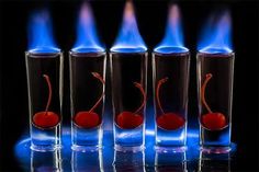 four glass vases with blue flames coming out of them and one has a cherry in it