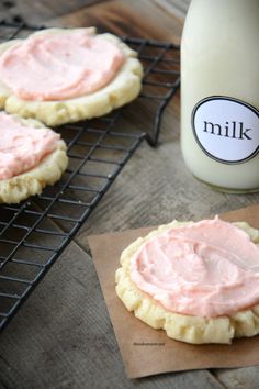 cookies with pink frosting sitting on a cooling rack next to a bottle of milk