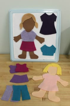 paper cutouts of children's clothes on a wooden table next to a mirror