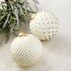 two white ornaments sitting on top of a table next to purple flowers and greenery