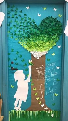 a door decorated with paper butterflies and a child's hand reaching up to a tree