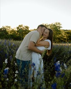 a man and woman embracing in a field of flowers at sunset with trees in the background