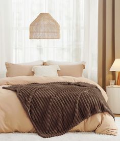 a bed with a brown blanket on top of it next to a lamp and window