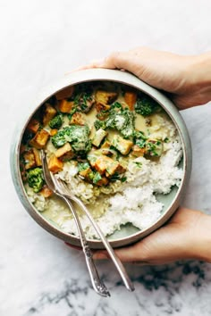 two hands holding a bowl filled with rice, broccoli and tofu