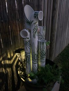 several white vases are stacked on top of each other in a planter next to a bamboo fence