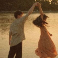 a man and woman are dancing on the beach at sunset with trees in the background