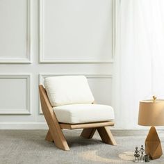 a white chair sitting next to a lamp on top of a wooden table in front of a wall