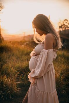 a pregnant woman is standing in the grass at sunset with her hands on her belly