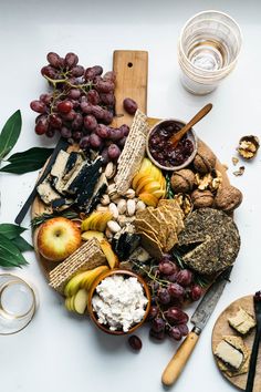 an assortment of cheeses, crackers and grapes on a board