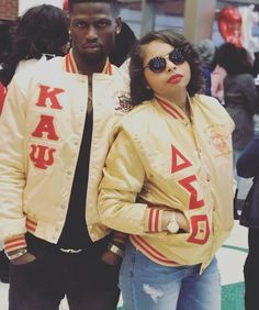 a man and woman standing next to each other in front of a crowd wearing jackets with letters on them