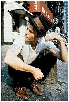 a man sitting on the side of a street next to a fire hydrant wearing a hat