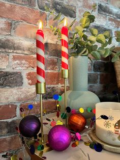 two candles are lit on a table with christmas decorations and other holiday items in front of a brick wall