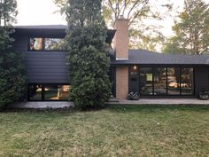 a modern house with large windows and trees in the front yard, surrounded by lush green grass