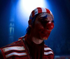 a man with clown makeup on his face wearing a red, white and blue striped vest