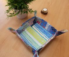 an empty patchwork tray sitting on top of a wooden table next to a potted plant