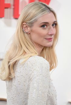 a woman with long blonde hair wearing earrings and a white dress at the red carpet event