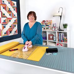 a woman is ironing fabric on a table with a quilter's block