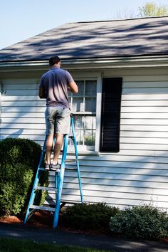 a man on a ladder painting the side of a house