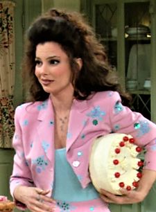 a woman holding a cake in her hand and wearing a pink suit with flowers on it