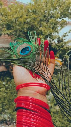 a woman's hand holding a peacock feather on top of her red bracelets