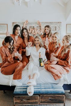 a group of women in orange robes sitting on a bed with champagne bottles and drinks