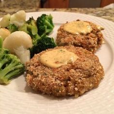 two crab cakes on a white plate with broccoli and potatoes next to it