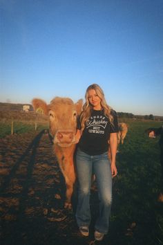 a woman standing next to a cow in a field