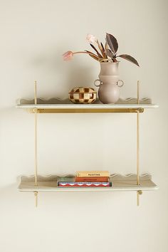 two shelves with vases, books and flowers on them in front of a white wall