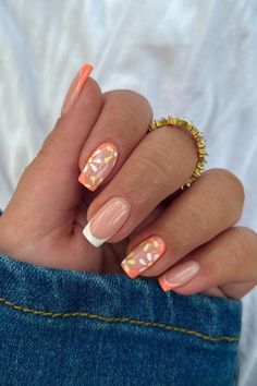 a woman's hand with orange and white manies on her nails, holding an orange ring