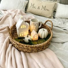 a wicker basket filled with white pumpkins and candles on top of a bed