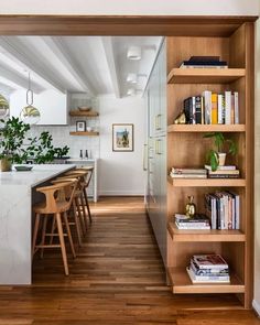 an open kitchen and dining room area with wooden flooring, white walls and shelves filled with books