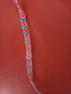 an orange, blue and pink crocheted cord on a red leather surface