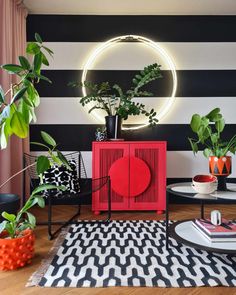 a living room with black and white stripes on the wall, red cabinet, potted plants, and round mirror