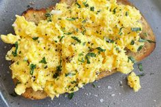 an open face sandwich with scrambled eggs on it and herbs sprinkled on top