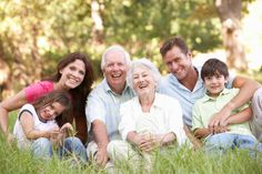 an older man, woman and two young children are sitting in the grass with their arms around each other