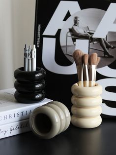 a stack of makeup brushes sitting on top of a table next to books and magazines