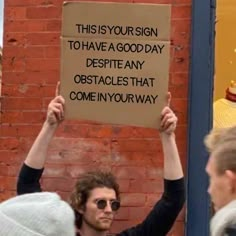 a man holding up a sign that says, this is your sign to have a good day despite obstacles that come in your way